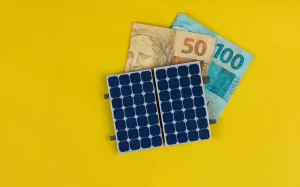 Conceito de payback energia solar: placas de energia fotovoltaica sobre fundo amarelo ao lado de notas de dinheiro de 50 e 100, sugerindo retorno do investimento em energia solar.