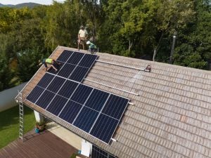 Equipe de instaladores posicionando painéis solares no telhado de uma casa, ilustrando a determinação da quantidade ideal de módulos fotovoltaicos para atender às necessidades de energia residencial e destacar como calcular o número correto de placas.