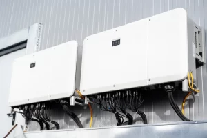 Inversores híbridos instalados em ambiente industrial, com unidades brancas sobre o painel e cabos de conexão visíveis, mostrando como funciona o sistema