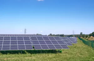 Maior projeto grid zero do Brasil: fileiras de painéis solares fotovoltaicos em grande escala MW, instalados em campo aberto com céu azul e postes de transmissão ao fundo.