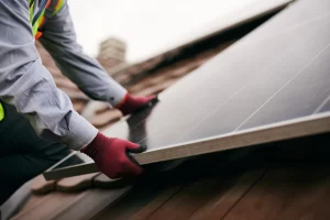 Trabalhador com luvas instalando módulos de energia solar fotovoltaica em telhado, fazendo fixação dos painéis, em contexto de conformidade com a NBR 16690 energia solar.