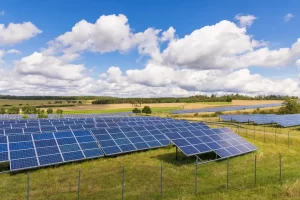 Campo com painéis solares fotovoltaicos instalados em fileiras, cercados por alambrado, sob céu azul com nuvens. Imagem que ilustra a viabilidade grid zero no ACL.