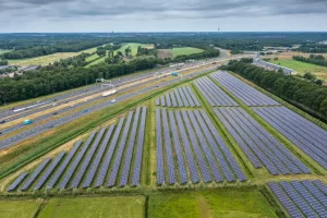 Vista aérea de um grande campo solar com fileiras de painéis fotovoltaicos instalados em meio a áreas verdes, ao lado de rodovias e construções, ilustrando um projeto de ampliar sistema solar homologado